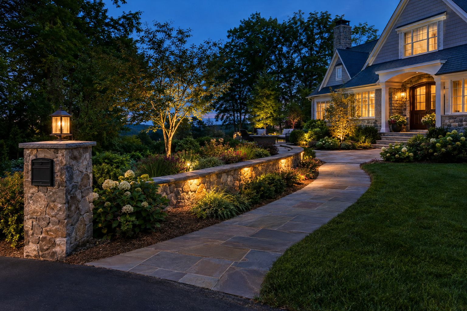 Stone walkway, lit retaining wall, and custom stone pillar mailbox with a lantern at dusk